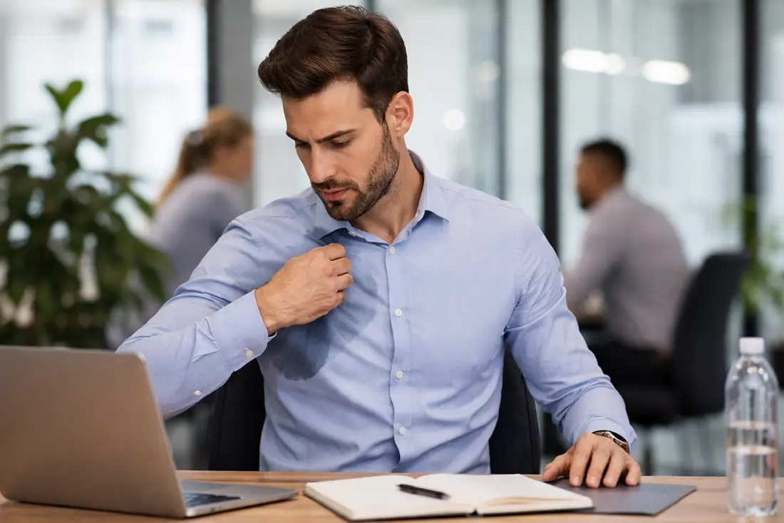Person experiencing excessive sweating at work in a professional office environment